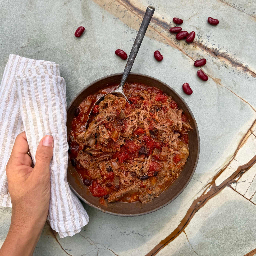 Bowl of pulled pork with beans on a marble surface