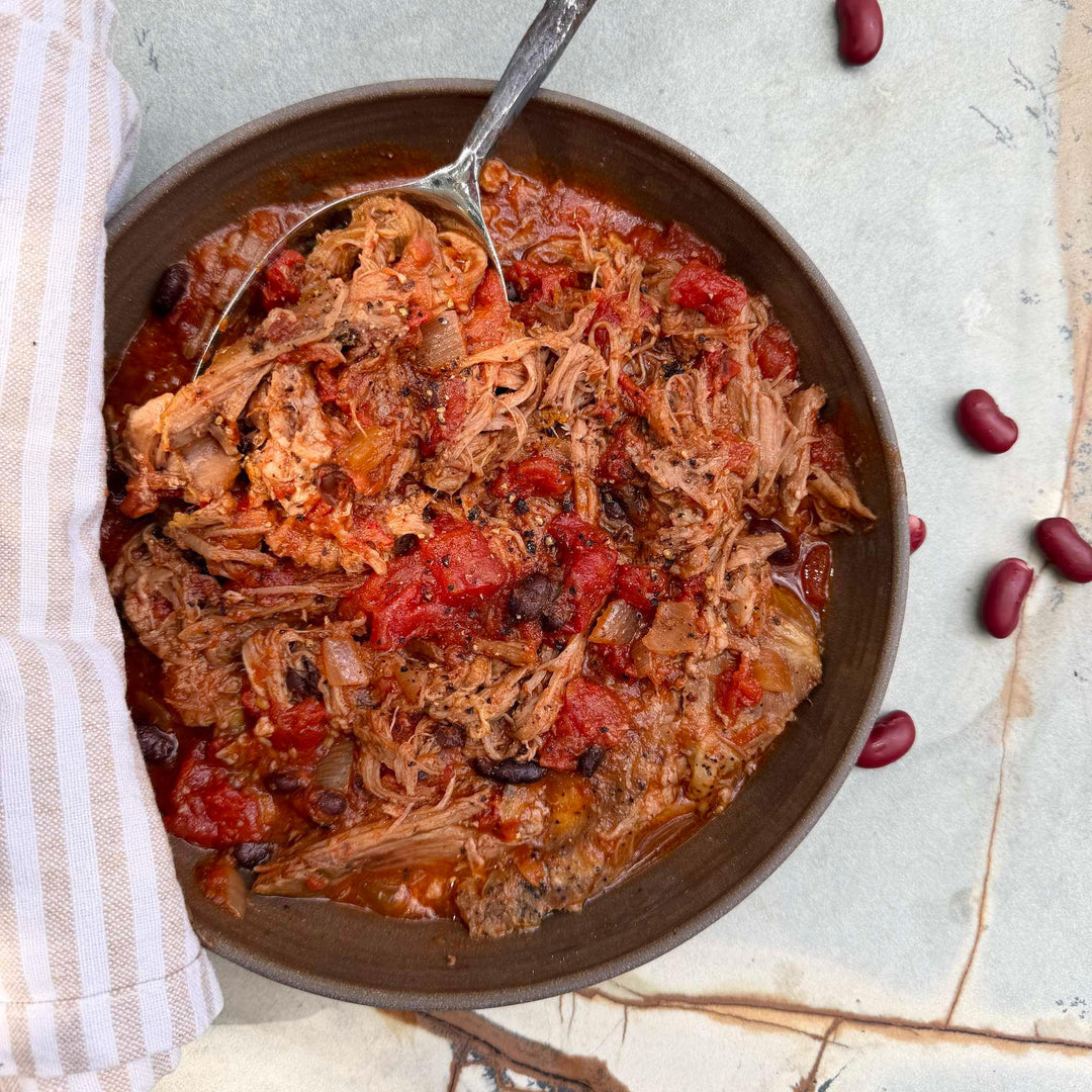 Bowl of pulled pork chili with a spoon on a light background