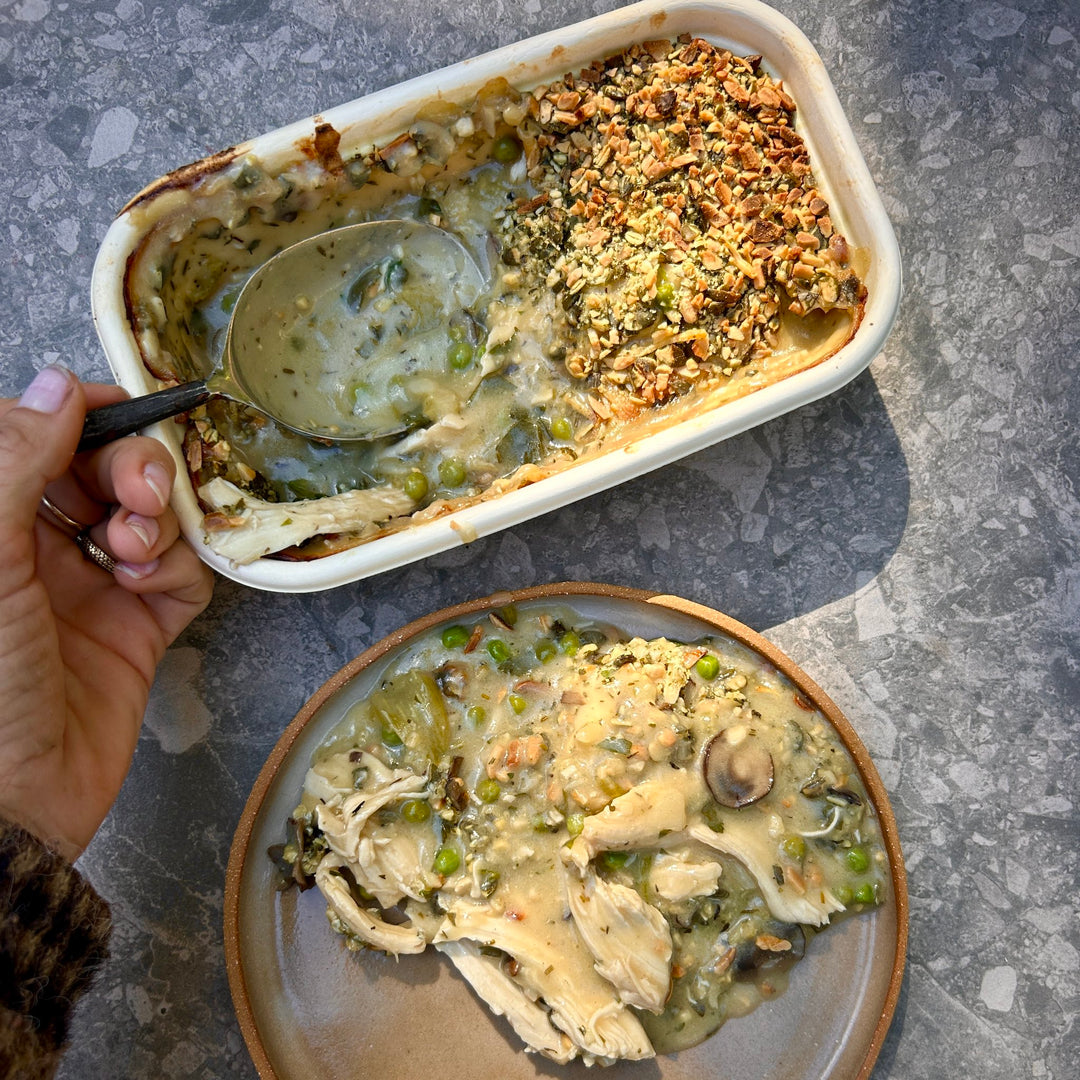 Baked chicken pie with a scoop taken out, showing a spoon and a plate of food on a gray surface.