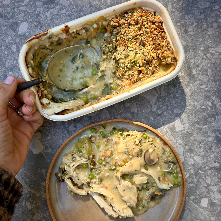 Baked chicken pie with a scoop taken out, showing a spoon and a plate of food on a gray surface.
