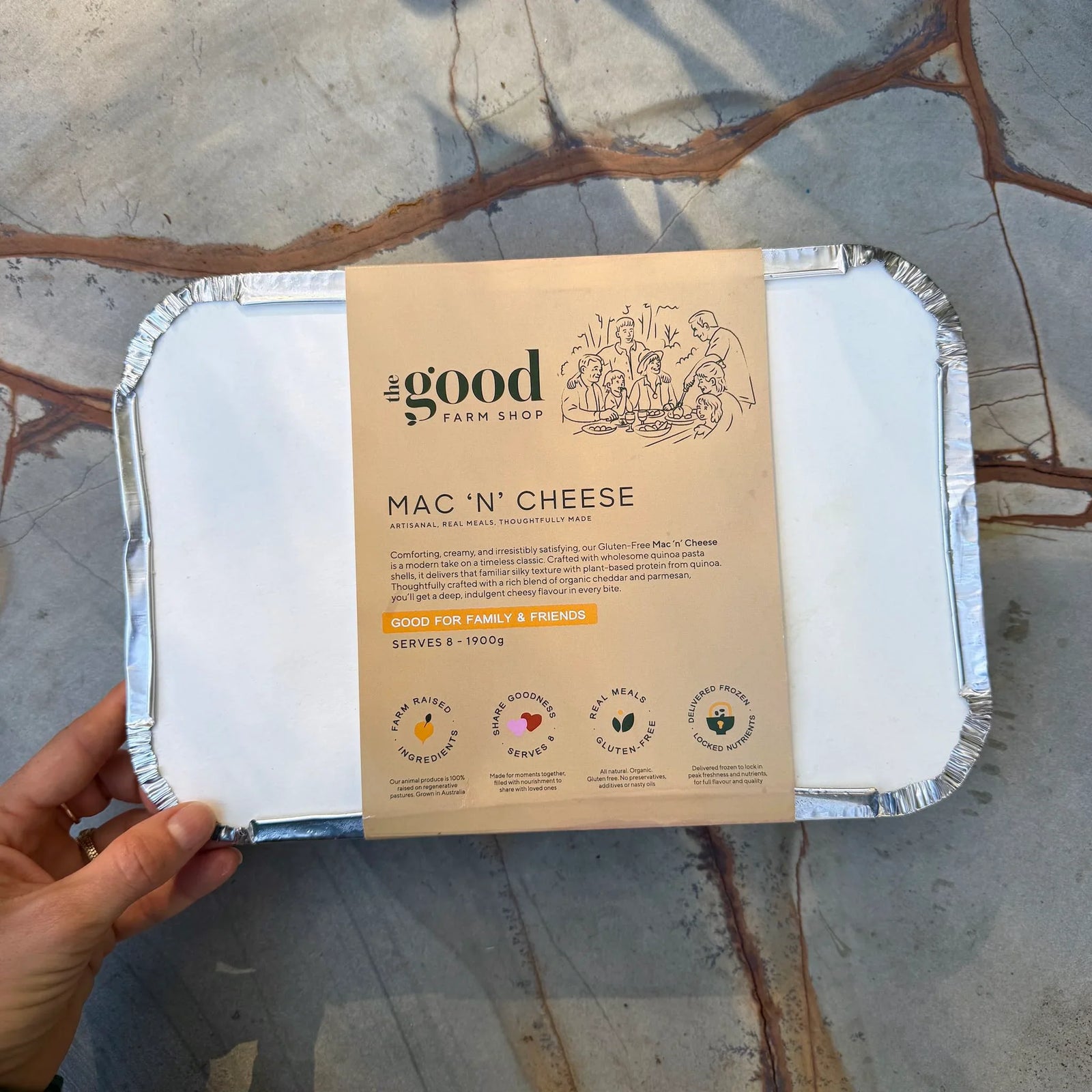 Mac 'n' Cheese packaging from the Good Farm Shop held by a hand on a stone surface.