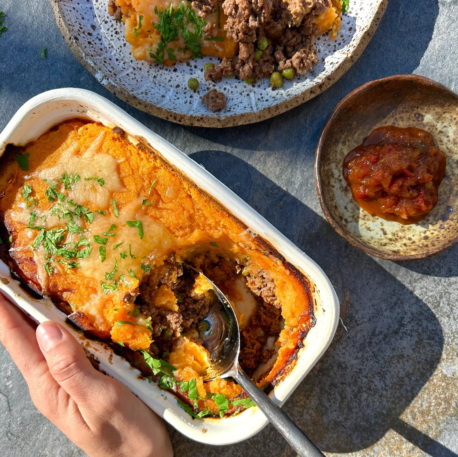 A serving of Shepherd's Pie in a white compostable container, with a spoonful taken out, showcasing the layers of lamb, vegetables, and mashed potatoes.