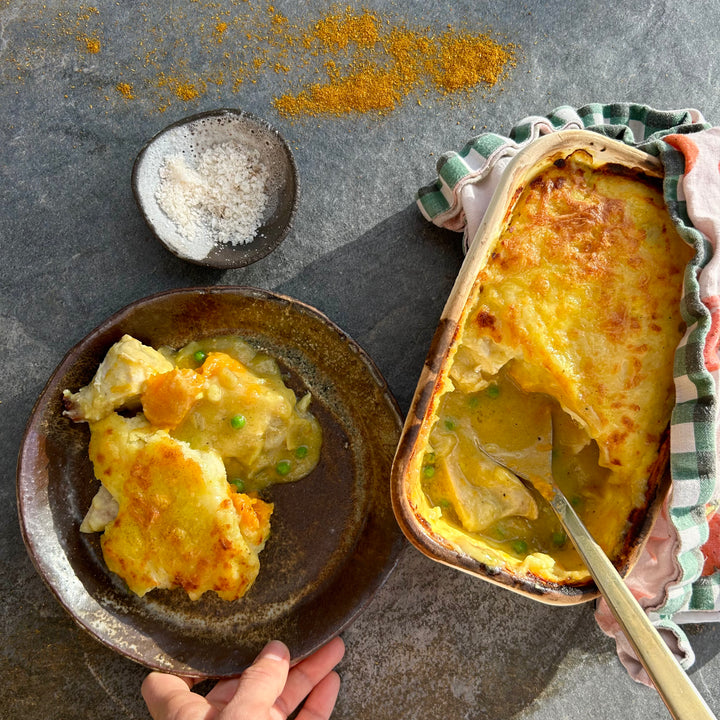 Hand holding plate of creamy chicken pie with mashed potato crust and peas and carrots