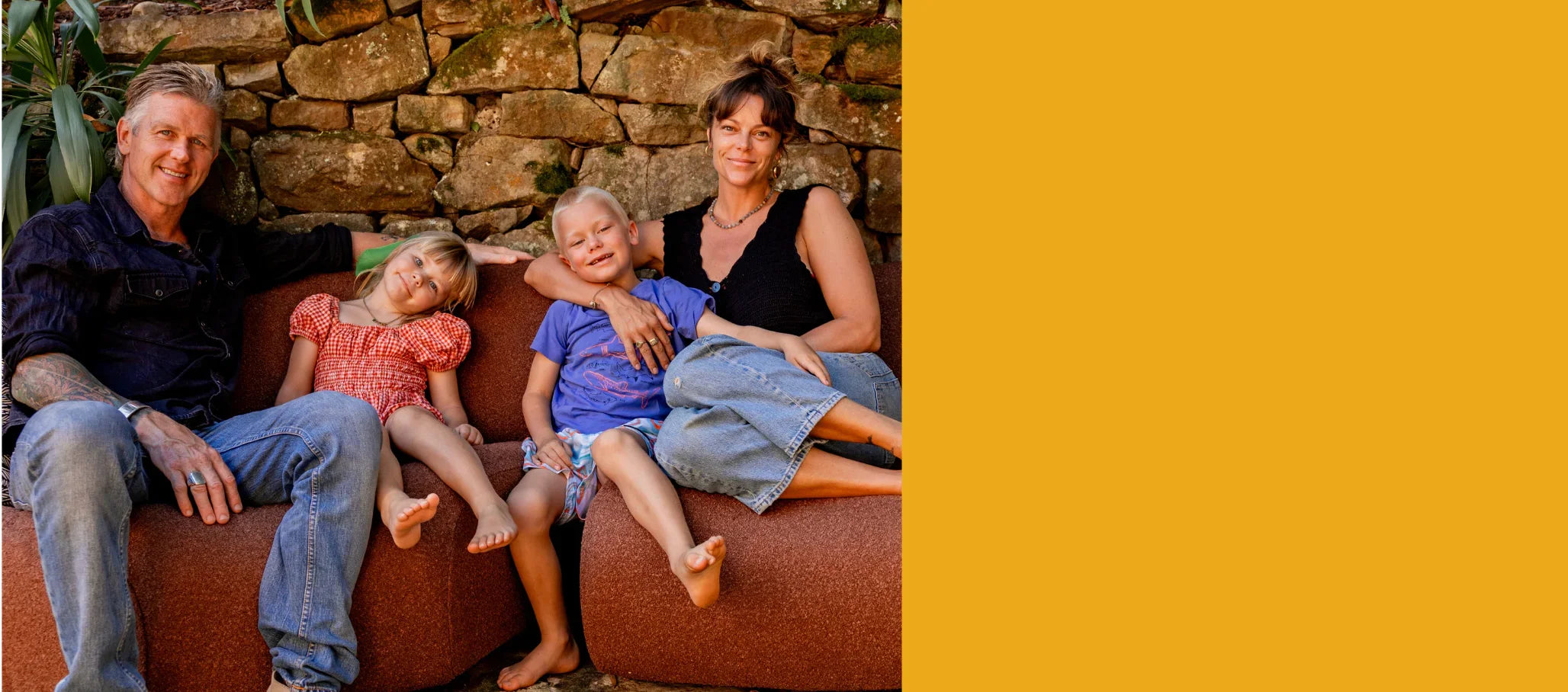 Family of four sitting on a brown couch against a stone wall.