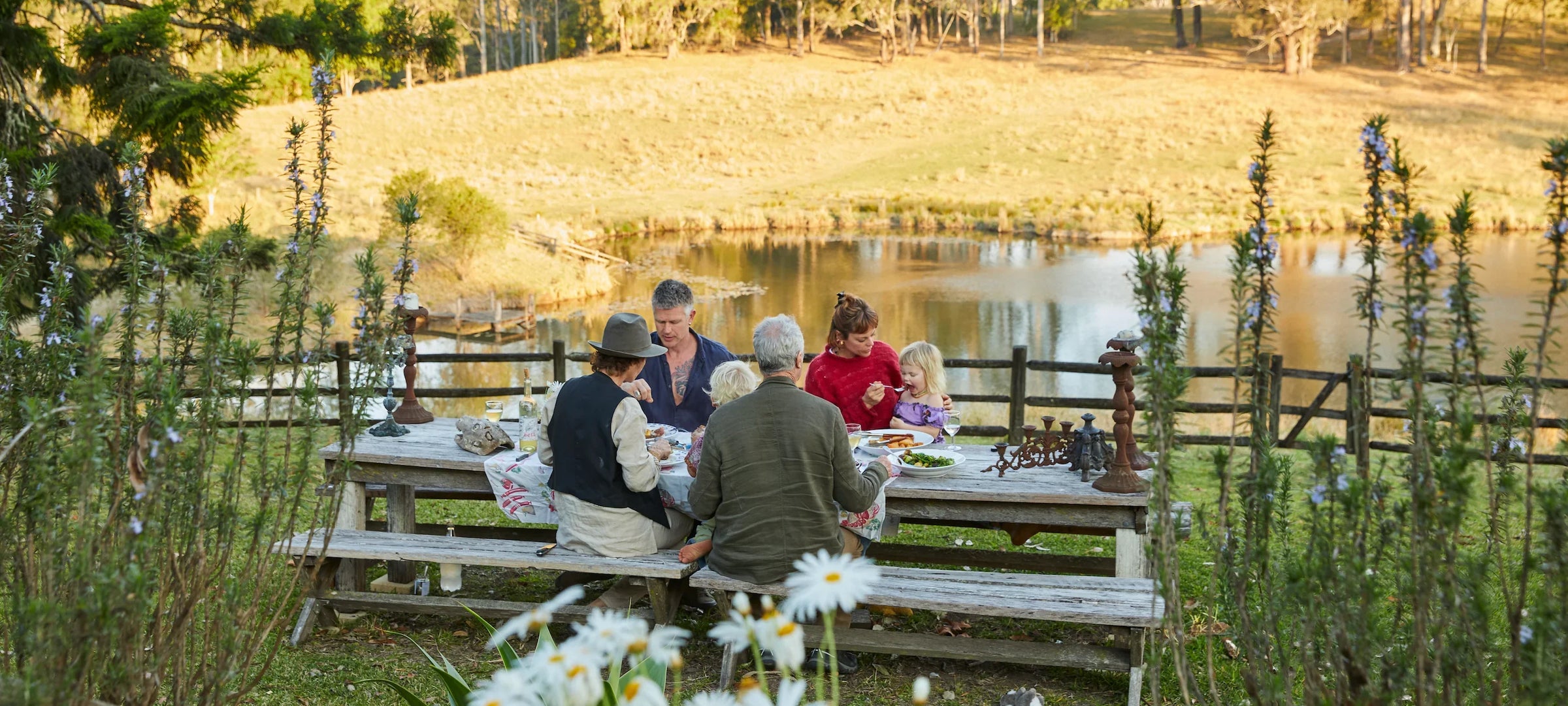 Family sitting at a picnic table by a lake with a scenic background