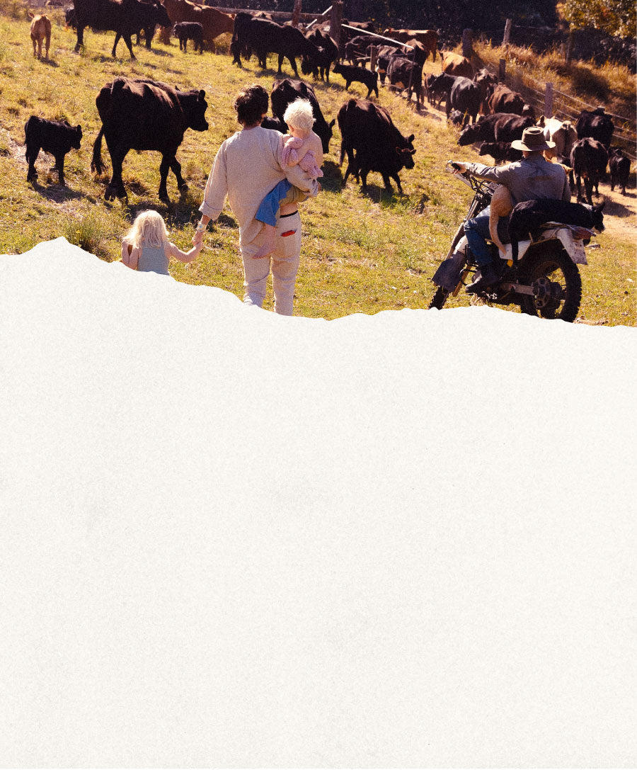 People with children and a motorcycle in a field with cows