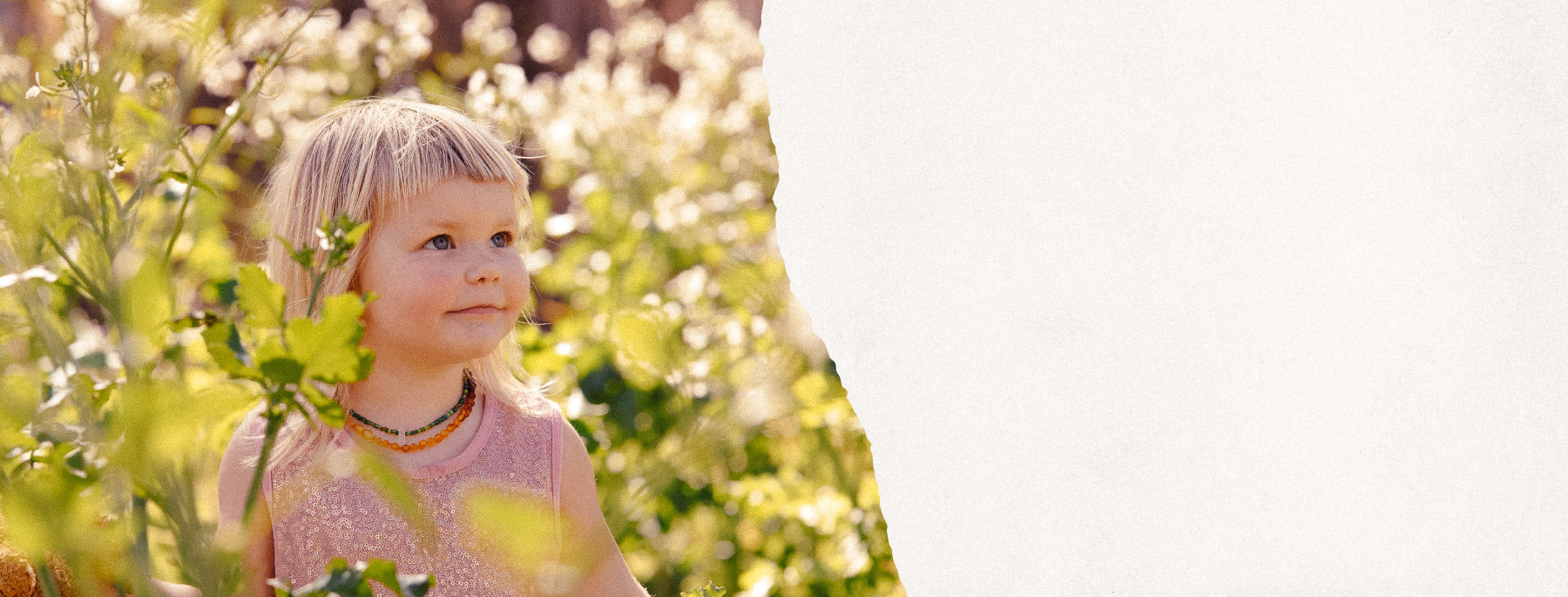 Child in a pink dress standing among greenery with a blurred background